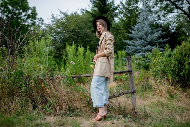 Stylish woman in hat and jacket in old countryside garden