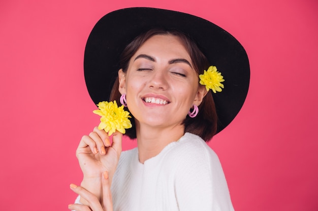 Stylish woman in hat, smiling with two yellow asters, spring mood, happy emotions isolated space bite lip