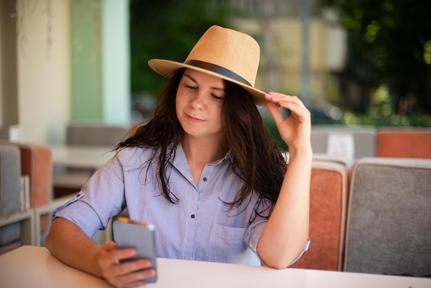 Stylish woman in hat with smartphone outsidemaking video call