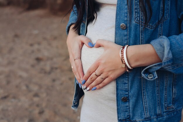 Stylish woman in jeans jacket holding palms on tummy