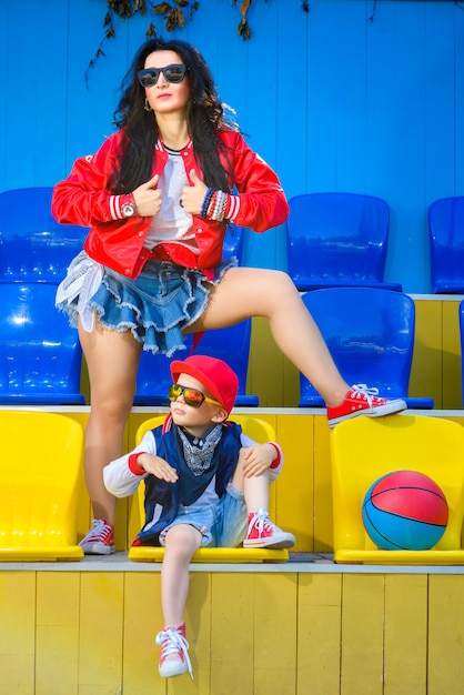 Stylish woman and little boy posing holding their feet on the ball at the basketball court