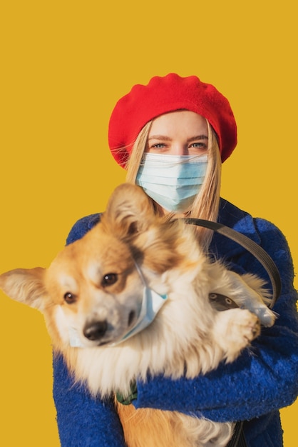 Stylish woman in a mask with a corgi dog in her arms