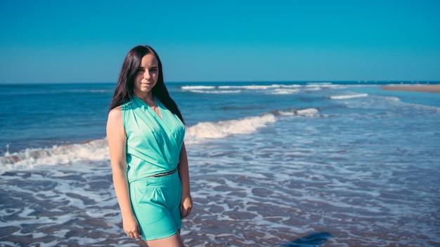 Stylish woman near waving sea Adult female in trendy summer outfit smiling and looking at camera while standing against waving sea and cloudless blue sky on resort