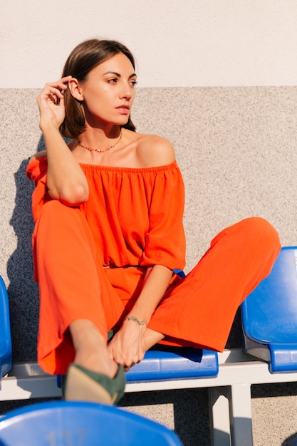 Donna alla moda in vestiti arancioni al tramonto alla posa dello stadio della pista ciclabile