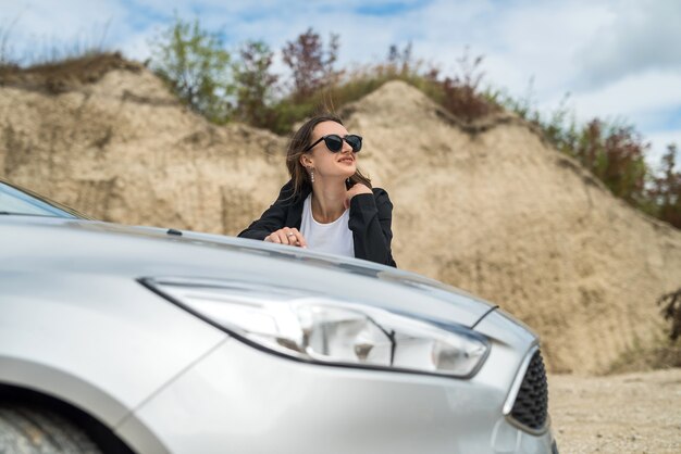 Donna alla moda in piedi vicino alla sua auto e godersi la libertà nella natura fuori città, ora legale