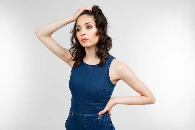 Stylish woman in summer blue denim overalls thinks on a white with copy space