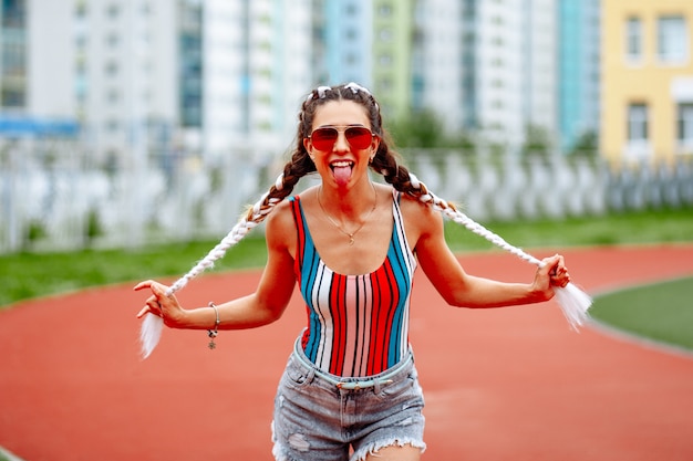 A stylish woman in sunglasses cheerfully poses against the background of the stadium.