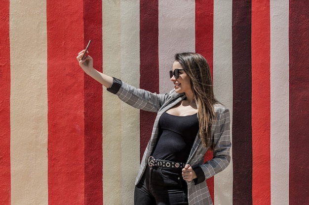 Stylish woman taking selfie in city on sunny day