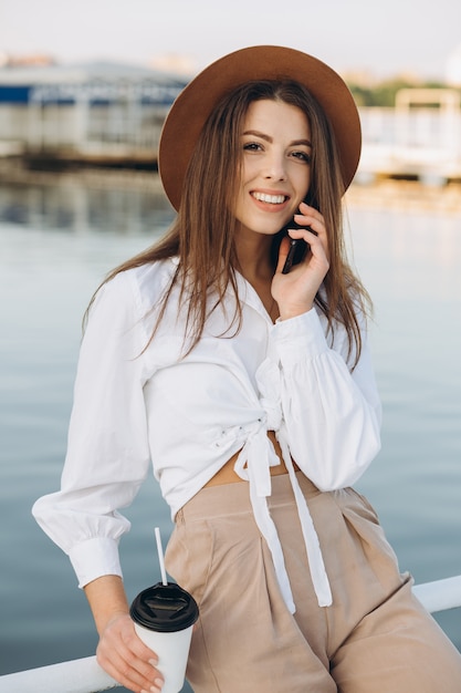 Una donna elegante parlando per telefono e camminando lungo la spiaggia in una calda giornata estiva al tramonto