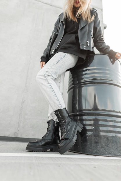 Stylish woman in trendy clothes with a fashionable leather jacket hoodie jeans and fashion leather black shoes near a black barrel on the street Women's spring style fashion and clothing