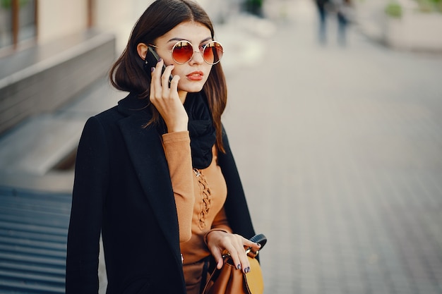 stylish woman uses her cell phone as she walks through the city on a sunny warm day