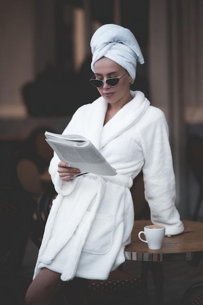 Стильная женщина в халате и банном полотенце держит свежий журнал