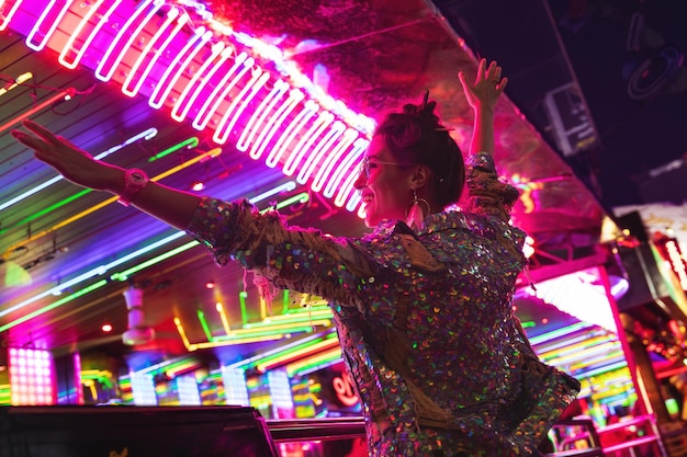 Stylish woman wearing jacket with shining sequins on the city street with neon lights