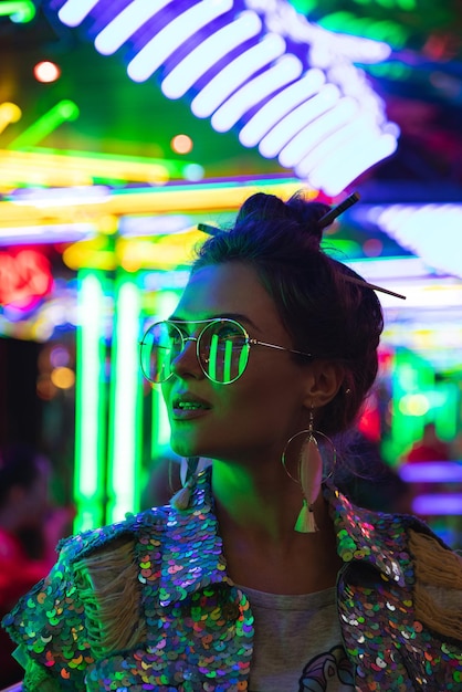 Stylish woman wearing jacket with shining sequins on the city street with neon lights