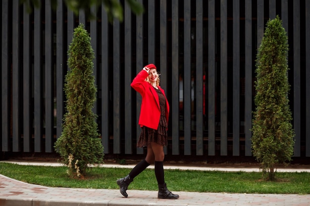 Donna alla moda che indossa berretto rosso e giacca abito scuro e stivali neri con ghette che camminano all'aperto