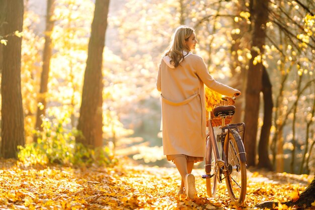 Stylish woman with bicycle enjoying autumn weather in the park Beautiful Woman in the autumn forest