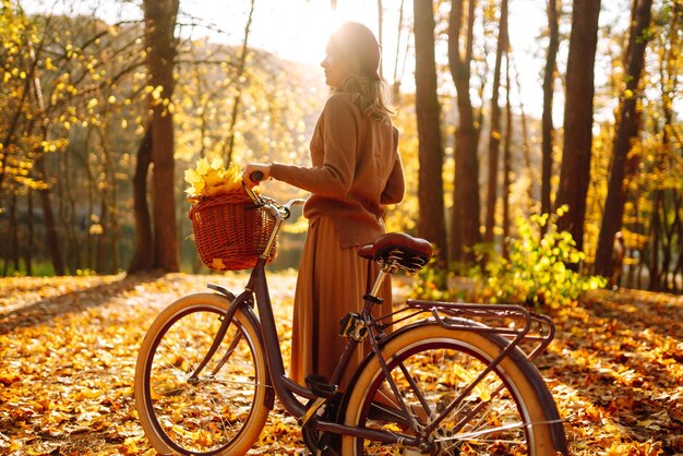 Stylish woman with bicycle enjoying autumn weather in the park Beautiful Woman in the autumn forest