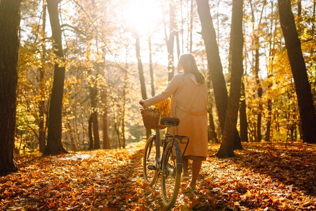 Stylish woman with bicycle enjoying autumn weather in the park Beautiful Woman in the autumn forest