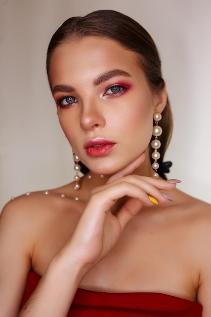 Stylish woman with makeup and in pearl earrings touching chin and looking at camera