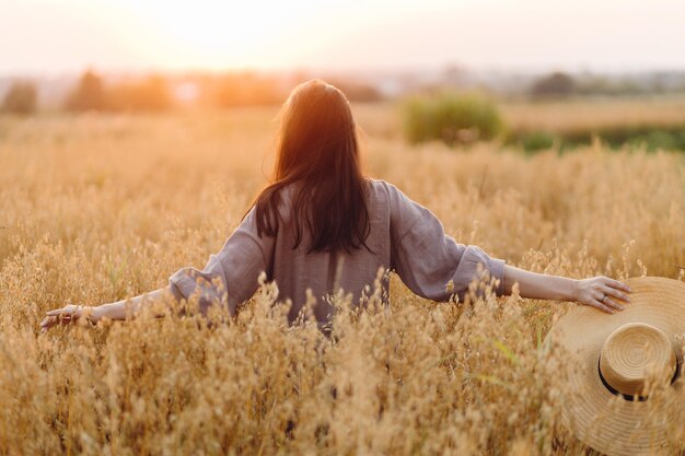夕日の光の中でエンバク畑に立つ麦わら帽子をかぶったスタイリッシュな女性大気の静かな瞬間