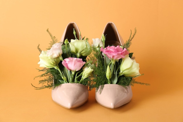 淡いオレンジ色の背景に美しい花を持つスタイリッシュな女性のハイヒールの靴