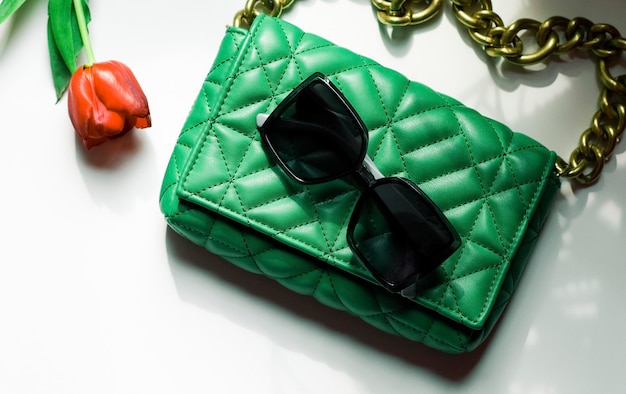 Stylish women's trendy green quilted bag with a large gold chain a red tulip in it and sunglasses