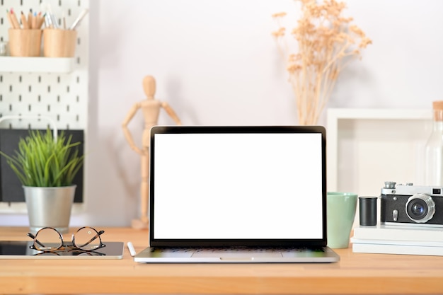 Stylish workplace desk blank screen laptop, vintage camera, poster and gadget