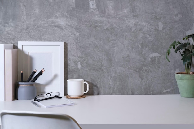 Stylish workplace with books coffee cup picture frame and potted plant on white table Copy space for your text