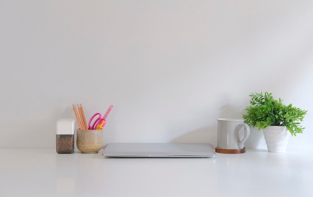 Stylish workplace with laptop stationery coffee cup and potted plant on white table