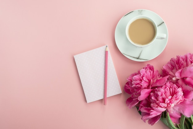 Foto elegante area di lavoro con tazza di caffè, blocco note e fiori di peonia rosa. tavolo da lavoro donna