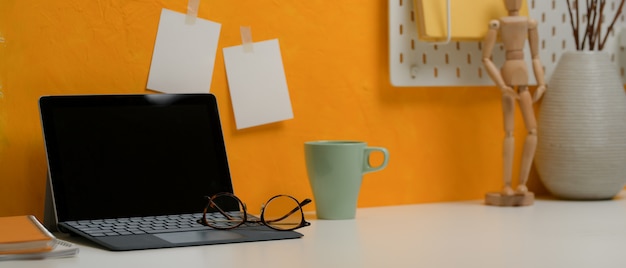 Фото Стильное рабочее пространство с цифровым планшетом, стаканами, кружкой и украшениями на белом столе