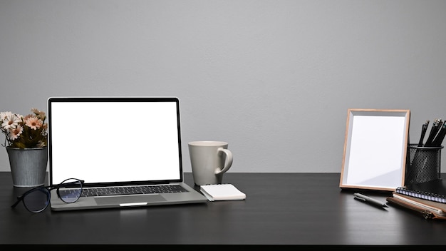 Stylish workspace with laptop computer picture frame and coffee cup on black table