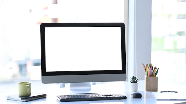 Elegante workstation con computer, tazza di caffè e forniture per ufficio sul tavolo bianco.