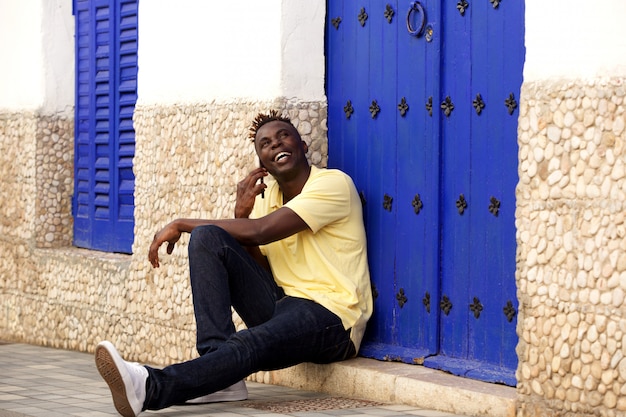 Stylish young african man sitting outside and talking on mobile phone