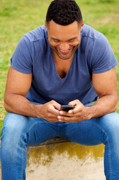 Foto elegante giovane uomo africano seduto fuori e utilizzando il telefono cellulare