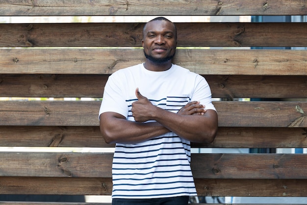 A stylish young AfricanAmerican man poses for the camera against the background of a wooden fence