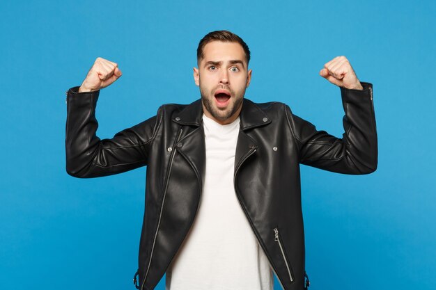 Stylish young bearded man in black leather jacket white t-shirt showing biceps, muscles isolated on blue wall background studio portrait. People sincere emotions lifestyle concept. Mock up copy space.