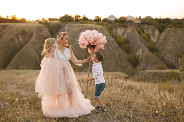 Stylish young boy gives a big flower to his mom in a field at sunset