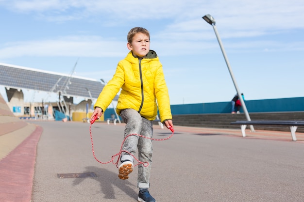 Stylish young boy teenager is jumping with skipping rope outdoors