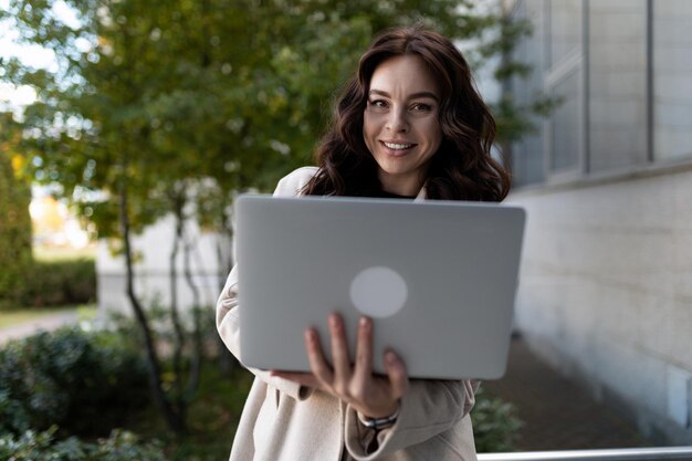 Photo stylish young business woman with a laptop in her hands against the backdrop of an office building