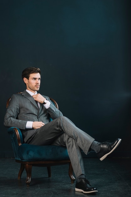 Photo stylish young businessman sitting on armchair against dark background