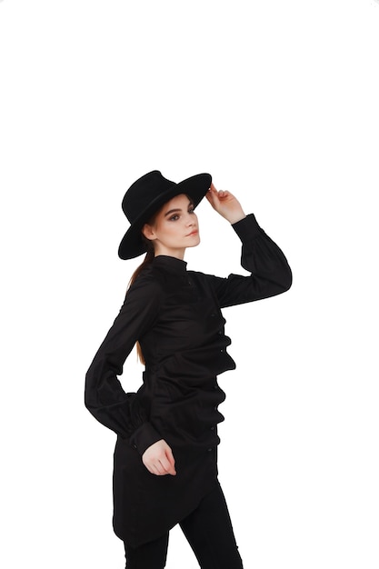 Stylish young businesswoman in black elegant suit and hat on white isolated background. Woman in fashionable clothes posing at camera. Concept of style, fashion, beauty and achievement of goals