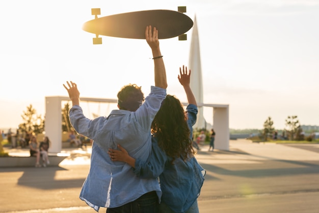 Stylish young couple hug looking at sunset hold skateboard happy girl and guy in love enjoy freedom