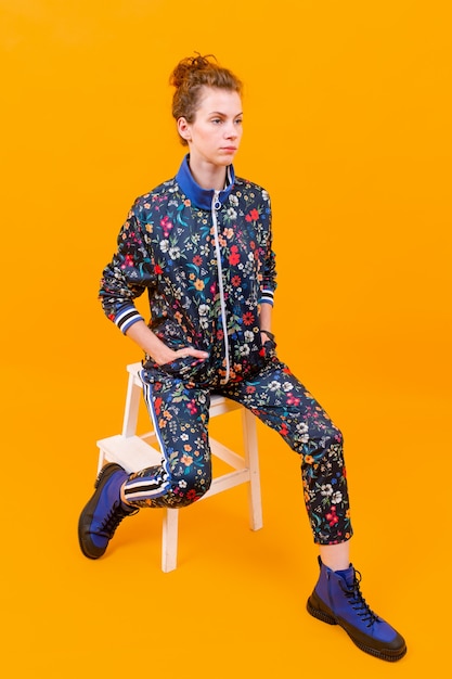 Stylish young girl posing on stepladder over orange background