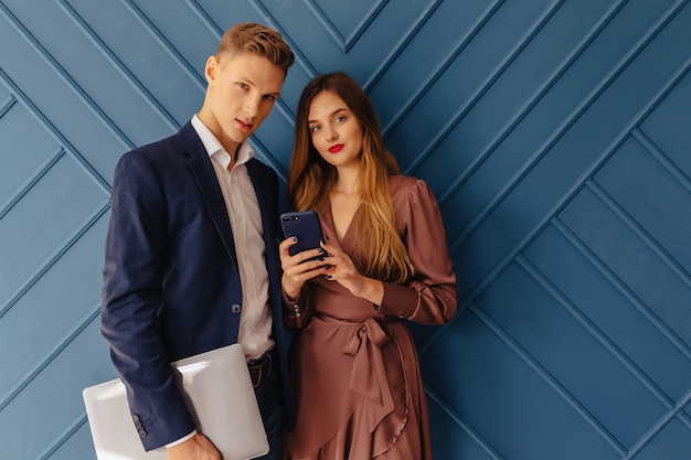 Stylish young guy with laptop and girl with phone emotions, aqua background
