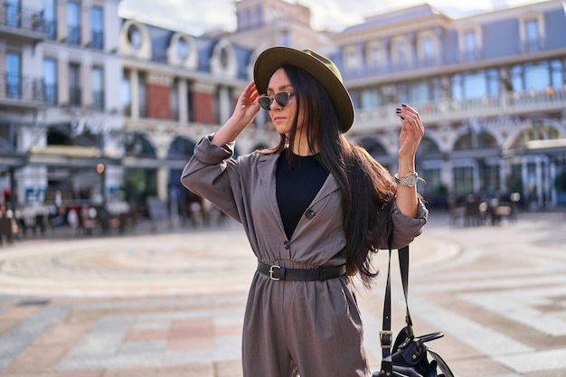 Stylish young hipster woman traveler wearing felt hat, sunglasses and overalls with a backpack