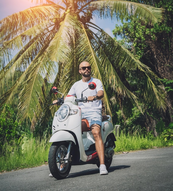 Стильный молодой человек и его мотоцикл на дороге в джунглях