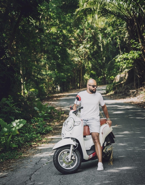 Stylish young man and his motorbike on the road in the jungle