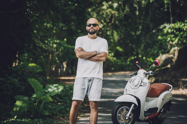 Stylish young man and his motorbike on the road in the jungle