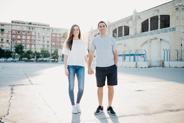 A stylish young man is holding hands with his brunette girlfriend in the port